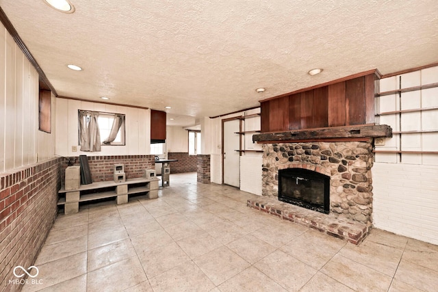 living room with light tile patterned floors, a stone fireplace, a textured ceiling, and brick wall