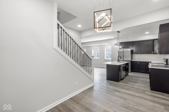 kitchen featuring a center island with sink, sink, backsplash, hanging light fixtures, and light wood-type flooring