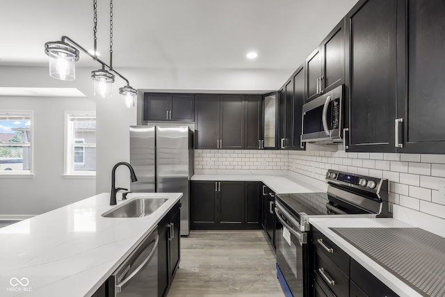 kitchen featuring appliances with stainless steel finishes, hanging light fixtures, decorative backsplash, sink, and light hardwood / wood-style floors