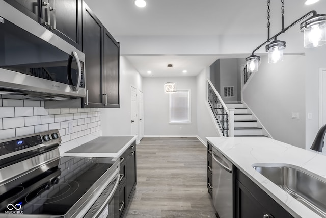 kitchen featuring stainless steel appliances, sink, light stone countertops, light hardwood / wood-style flooring, and decorative light fixtures