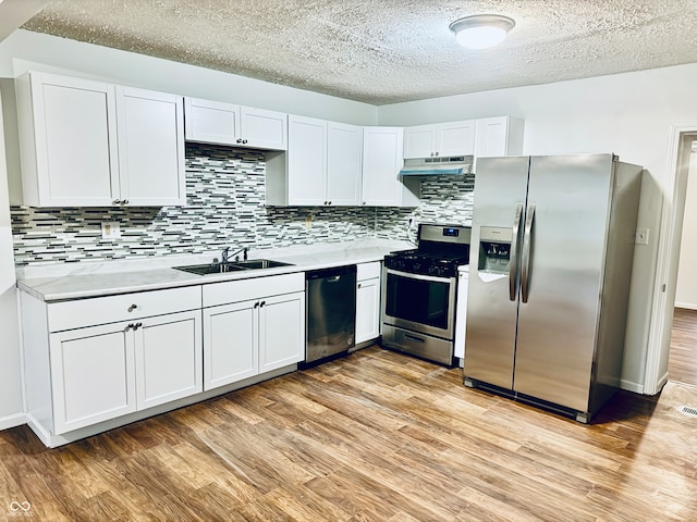 kitchen with white cabinets, sink, light wood-type flooring, appliances with stainless steel finishes, and tasteful backsplash