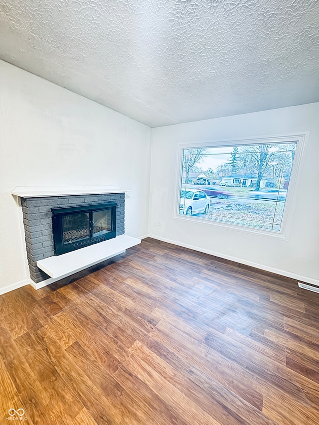 unfurnished living room featuring hardwood / wood-style floors, a textured ceiling, and a brick fireplace