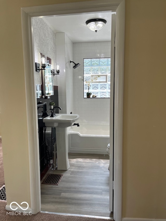 bathroom with wood-type flooring, toilet, and tiled shower / bath