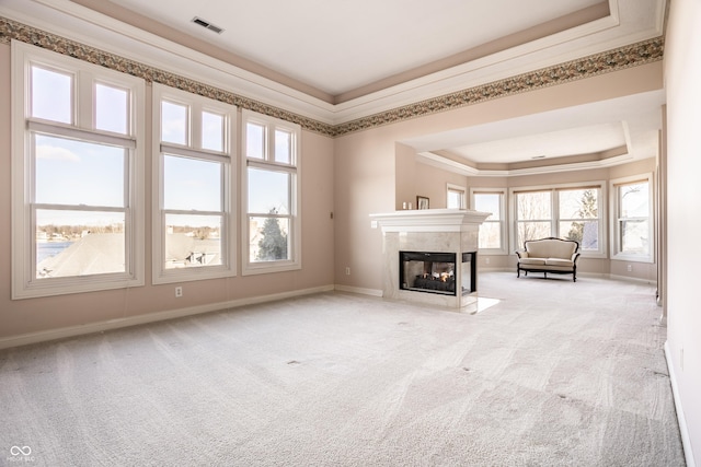 unfurnished living room with a raised ceiling, crown molding, a multi sided fireplace, and light carpet