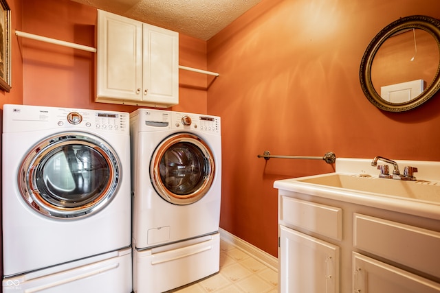 laundry room featuring washing machine and dryer, sink, cabinets, and a textured ceiling