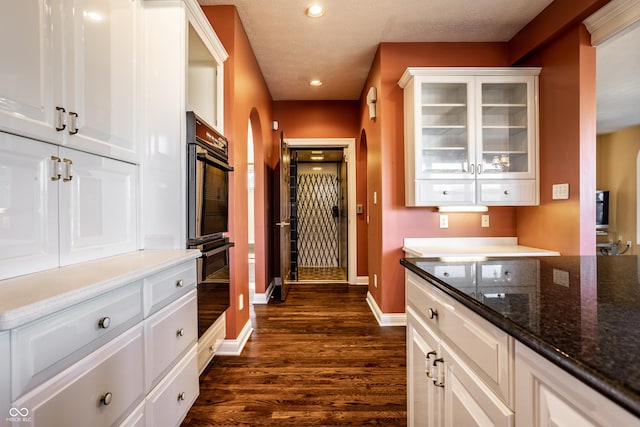 kitchen featuring double oven, dark stone countertops, white cabinetry, and dark hardwood / wood-style flooring