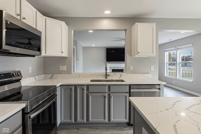 kitchen with light stone countertops, gray cabinetry, stainless steel appliances, sink, and white cabinetry