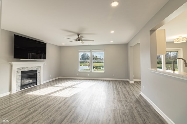 unfurnished living room with a stone fireplace, ceiling fan, a healthy amount of sunlight, and wood-type flooring