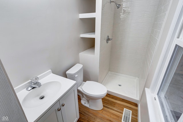 bathroom with hardwood / wood-style floors, vanity, toilet, and tiled shower