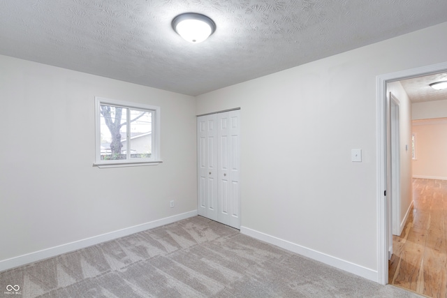 unfurnished bedroom featuring light colored carpet, a textured ceiling, and a closet