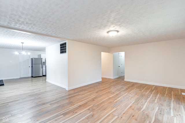 empty room featuring light wood-type flooring, a textured ceiling, and an inviting chandelier