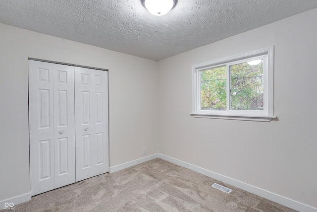 unfurnished bedroom featuring light carpet, a closet, and a textured ceiling