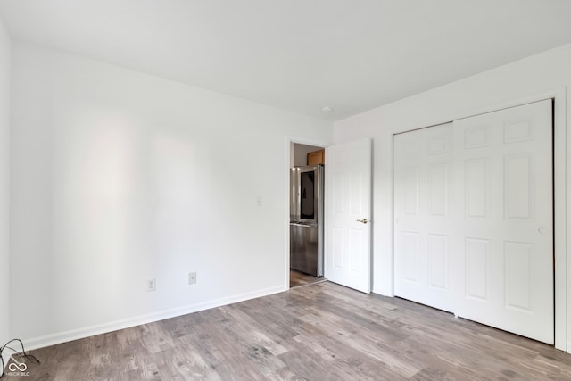 unfurnished bedroom with smart refrigerator, wood finished floors, baseboards, and a closet