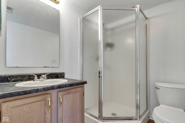 bathroom featuring toilet, vanity, a textured ceiling, and a shower with door