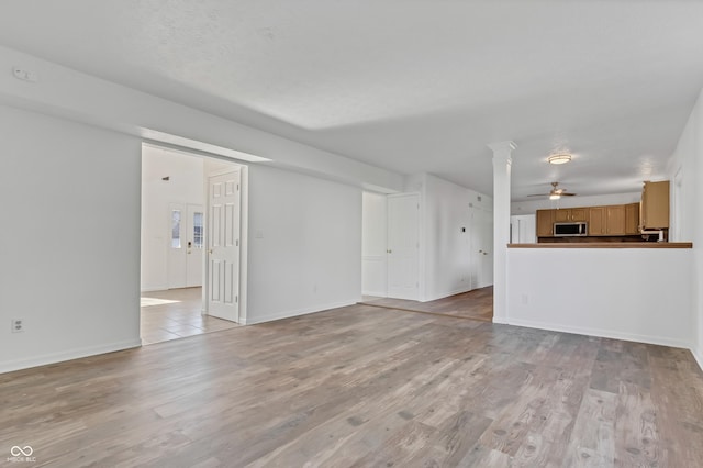 unfurnished living room with light wood-type flooring, ceiling fan, and baseboards