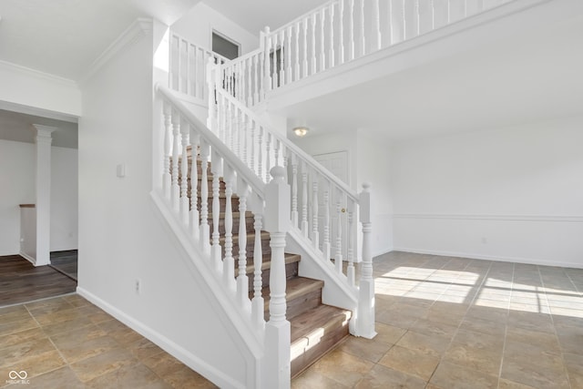 staircase featuring stone finish floors, baseboards, crown molding, and a towering ceiling