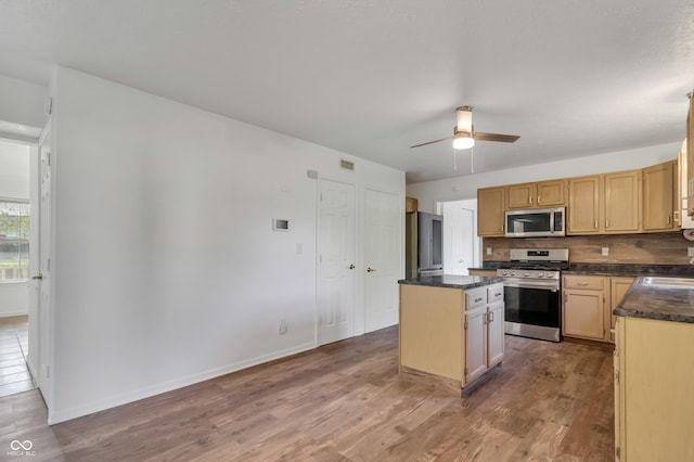 kitchen featuring stainless steel appliances, dark countertops, a kitchen island, and wood finished floors