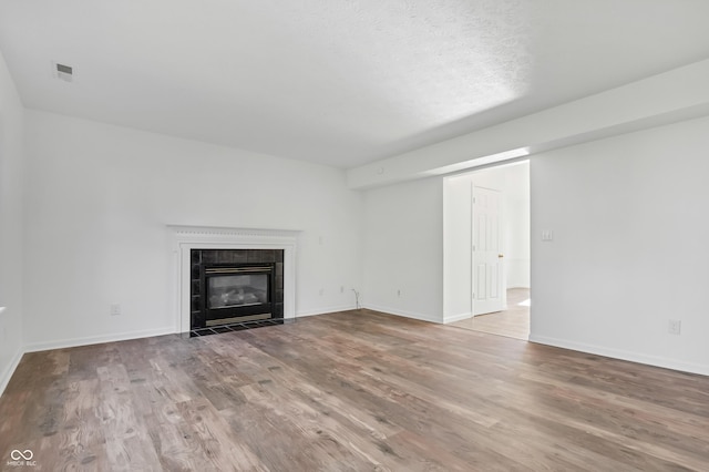 unfurnished living room featuring wood finished floors, a tiled fireplace, and baseboards