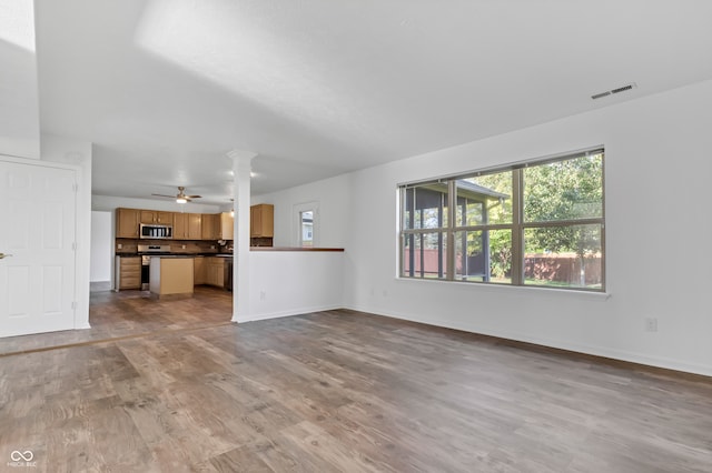 unfurnished living room with ceiling fan, hardwood / wood-style floors, and ornate columns