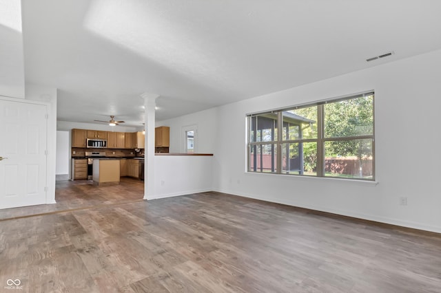 unfurnished living room featuring wood finished floors, baseboards, ceiling fan, and decorative columns