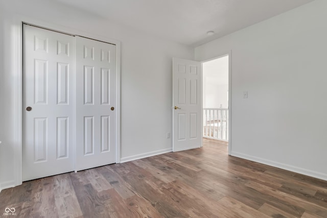 unfurnished bedroom with wood finished floors, baseboards, and a closet