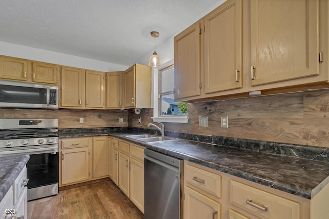 kitchen with appliances with stainless steel finishes, a sink, light wood-style flooring, dark countertops, and backsplash