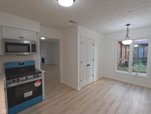 kitchen with light wood-type flooring, appliances with stainless steel finishes, a textured ceiling, pendant lighting, and white cabinets