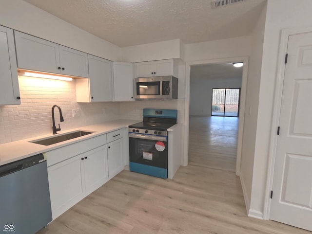 kitchen featuring white cabinetry, sink, appliances with stainless steel finishes, a textured ceiling, and light hardwood / wood-style flooring