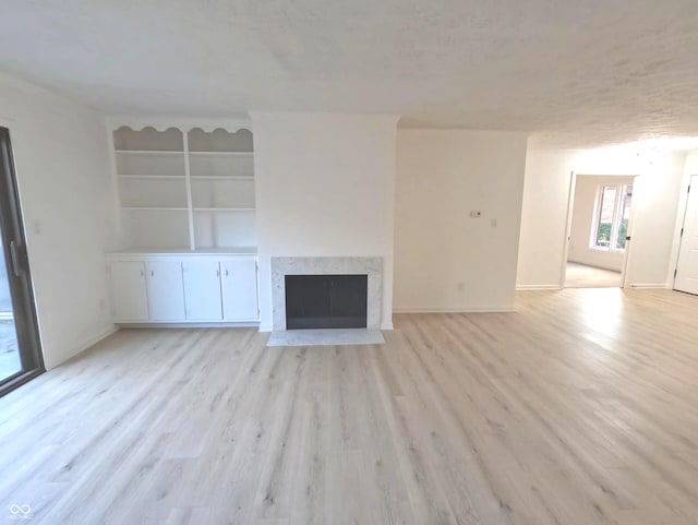 unfurnished living room featuring light wood-type flooring, built in features, a textured ceiling, and a high end fireplace