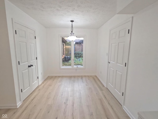 unfurnished dining area featuring light wood-type flooring and a textured ceiling