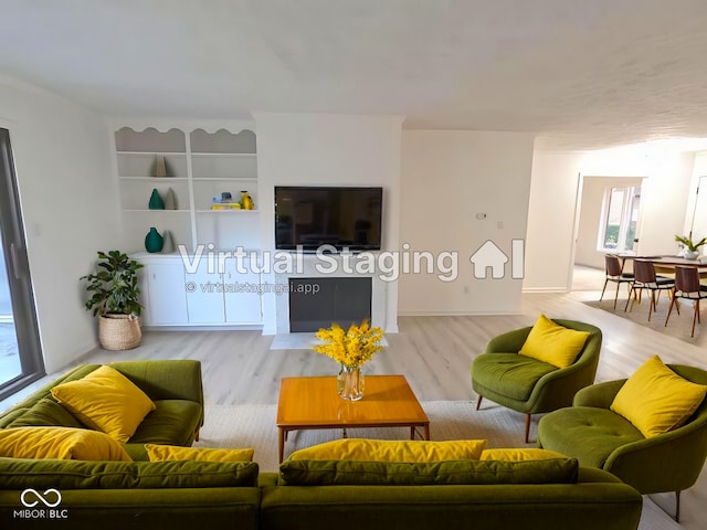 living room featuring built in shelves, light wood-type flooring, and plenty of natural light