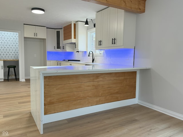 kitchen with white cabinetry, backsplash, light wood-type flooring, gas cooktop, and kitchen peninsula