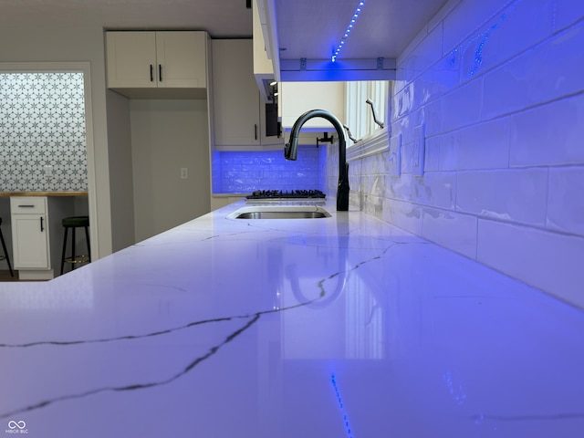 room details featuring decorative backsplash, white cabinetry, sink, and light stone counters