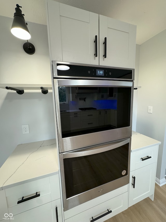 room details featuring light hardwood / wood-style floors, light stone counters, hanging light fixtures, double oven, and white cabinets