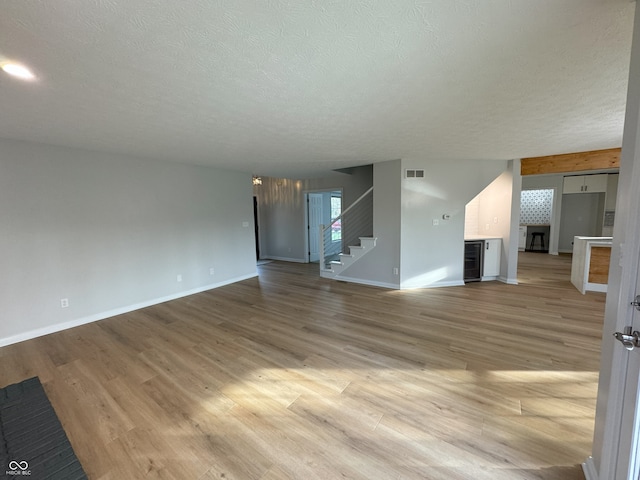 unfurnished living room with beverage cooler, light wood-type flooring, and a textured ceiling