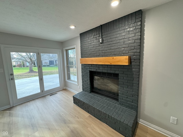 unfurnished living room with a brick fireplace, light hardwood / wood-style floors, plenty of natural light, and a textured ceiling