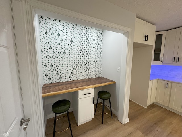 office area with a textured ceiling, built in desk, and light hardwood / wood-style flooring