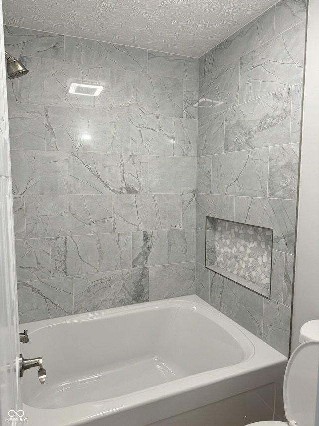 bathroom featuring toilet, tiled shower / bath, and a textured ceiling