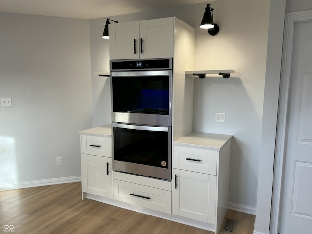 kitchen featuring white cabinets, light wood-type flooring, decorative light fixtures, and double oven