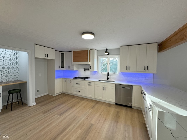 kitchen with backsplash, sink, light hardwood / wood-style floors, white cabinets, and stainless steel dishwasher