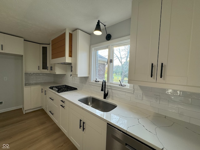 kitchen with sink, light stone countertops, light hardwood / wood-style flooring, white cabinets, and decorative backsplash