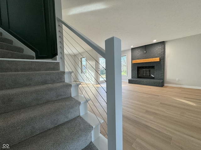 staircase with a brick fireplace, wood-type flooring, and a textured ceiling