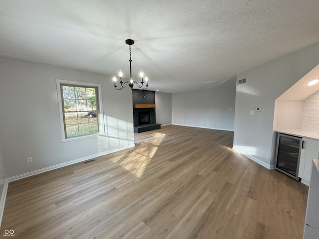 unfurnished living room featuring a fireplace, wine cooler, a textured ceiling, a notable chandelier, and light hardwood / wood-style flooring