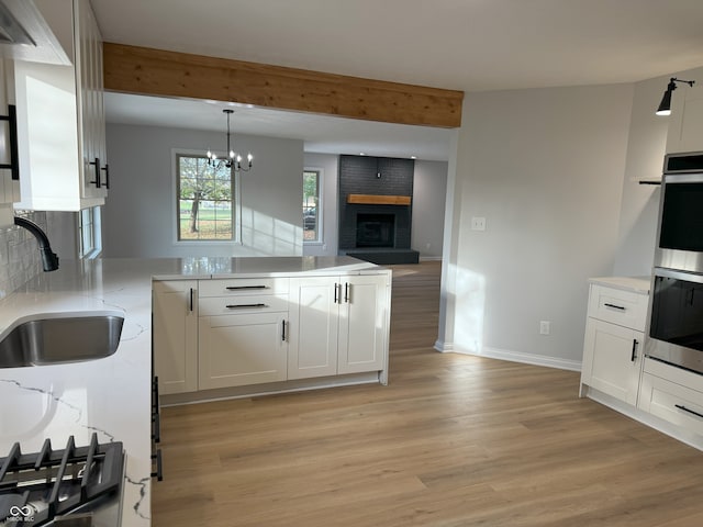 kitchen featuring white cabinets, sink, light hardwood / wood-style floors, a brick fireplace, and a chandelier