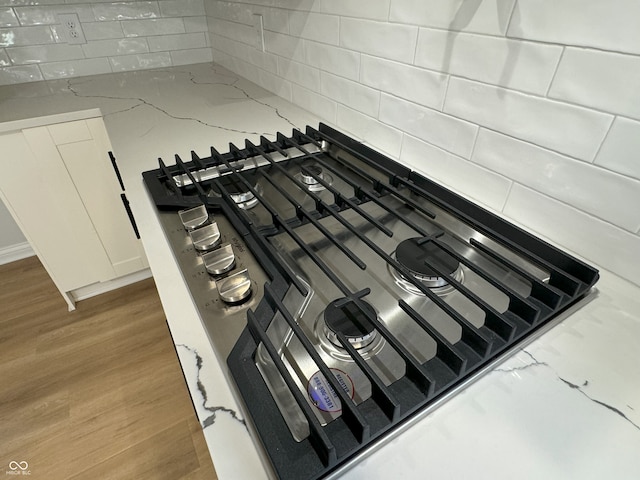 details with light stone countertops, wood-type flooring, white cabinetry, and black gas stovetop