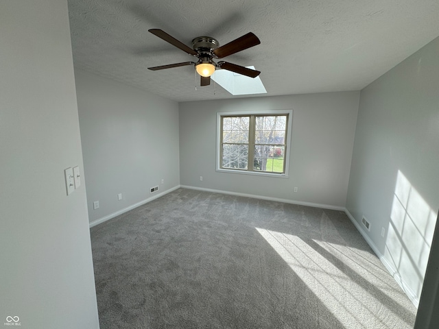 carpeted spare room with a textured ceiling, ceiling fan, and a skylight