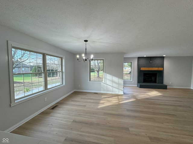 unfurnished dining area featuring a fireplace, light hardwood / wood-style flooring, a notable chandelier, and a textured ceiling