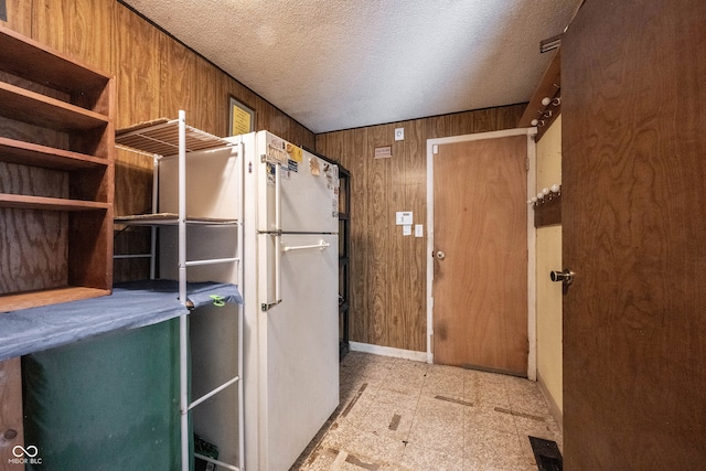 interior space with wooden walls, a textured ceiling, and white fridge