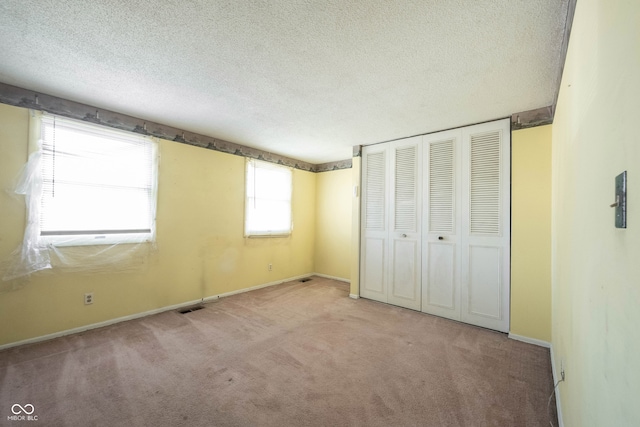 unfurnished bedroom featuring a closet, a textured ceiling, and light colored carpet