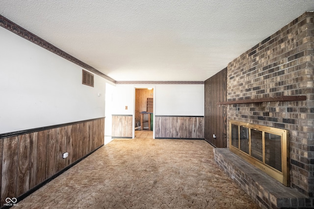 unfurnished living room featuring wood walls, ornamental molding, a textured ceiling, a fireplace, and light colored carpet